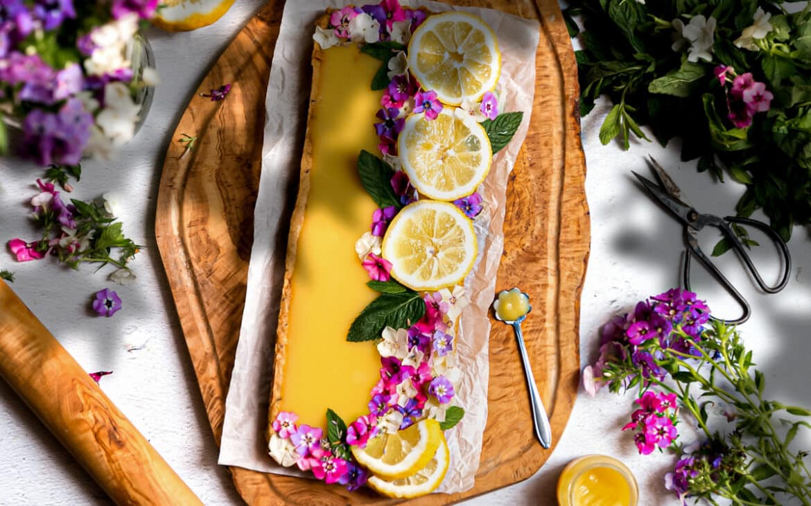 Lavender lemon tart with flowers and sliced lemons on a wooden background.