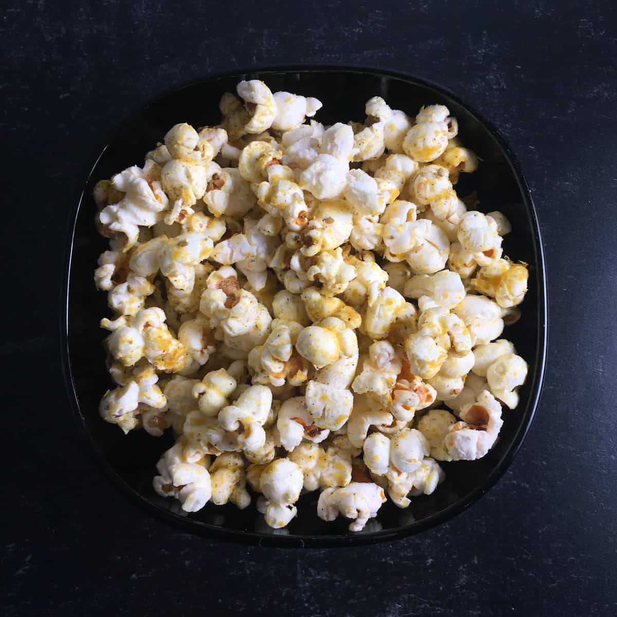Za'atar popcorn recipe on a black plate on a black background.