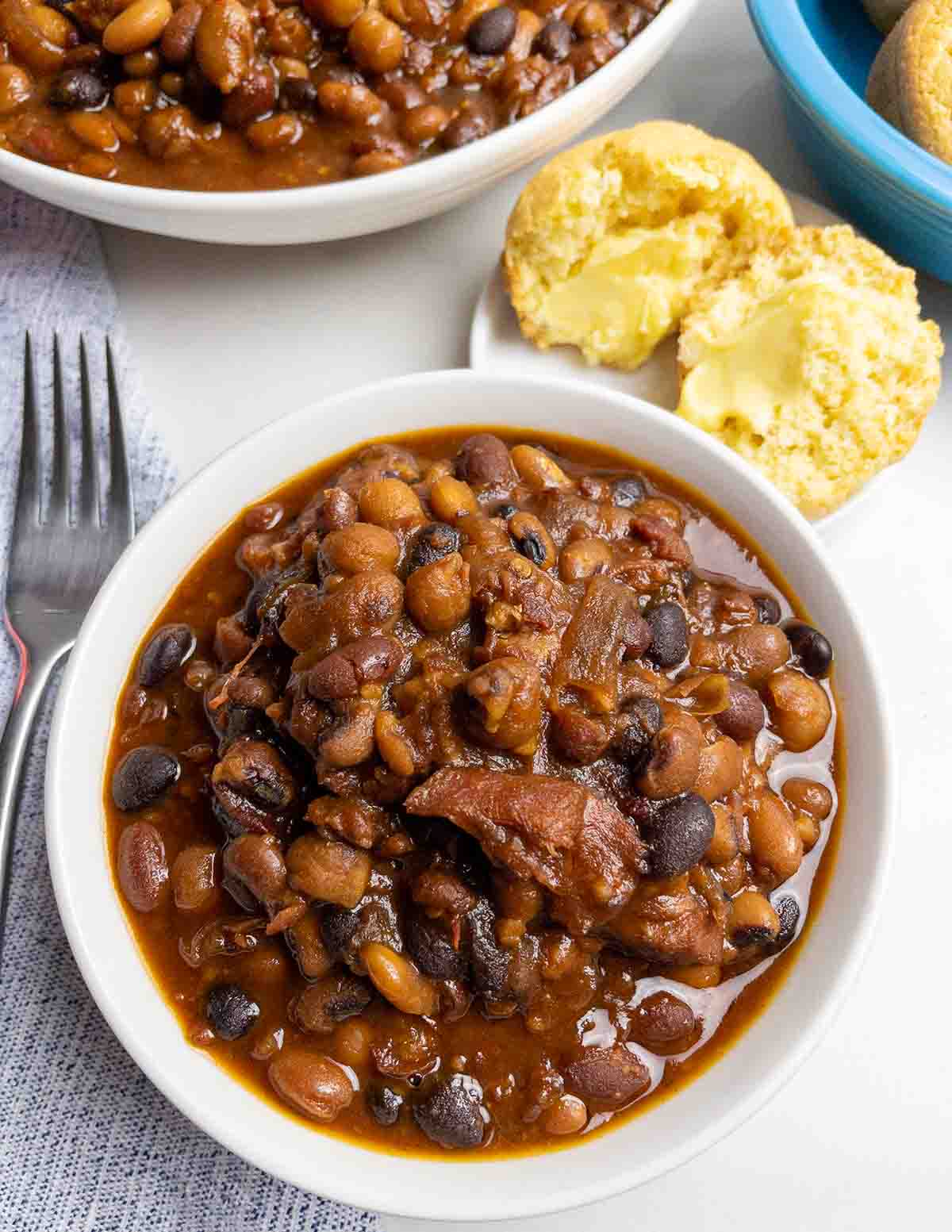 Slow cooker baked beans with ham in a white bowl with cornbread.