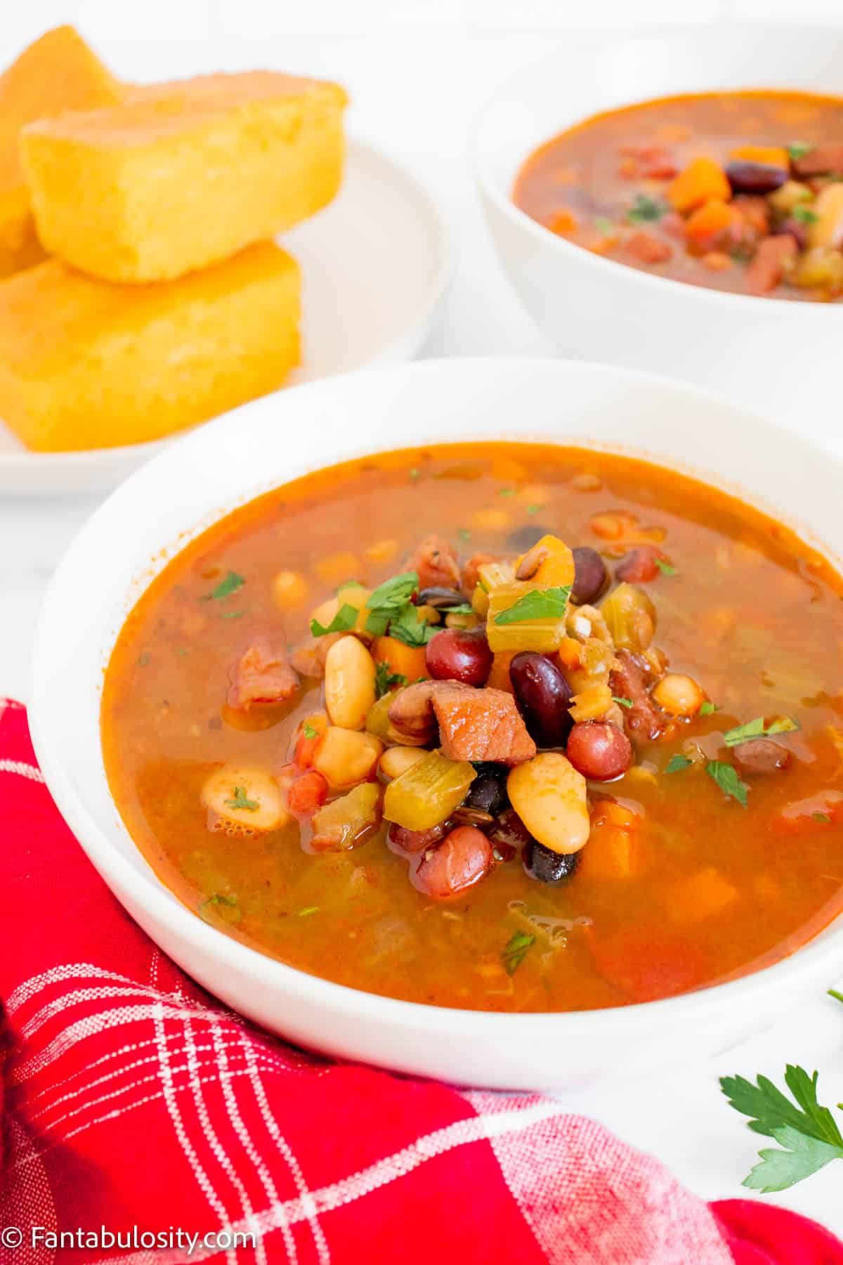 15 bean soup in white bowls with a stack of cornbread in background.