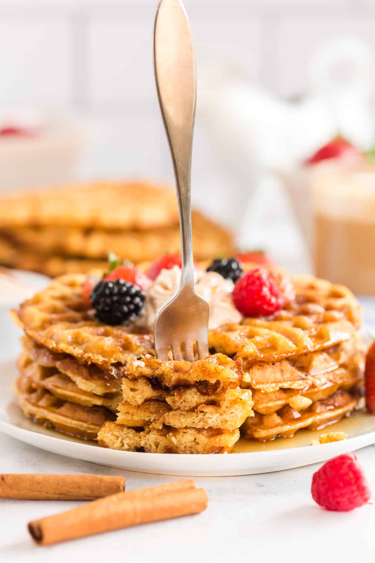 Stack of buttermilk cornbread waffles with berries and whipped cream with a fork.