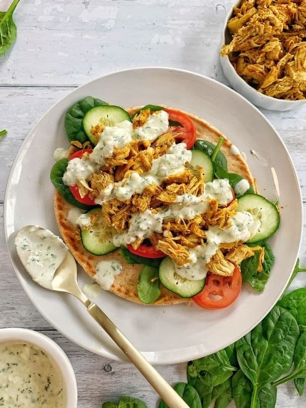 Instant pot chicken shawarma wraps with spinach, tomato, cucumber, and sauce on a plate.