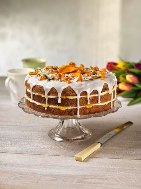 Coconut mango lime cake on a clear cake stand with a cake knife.