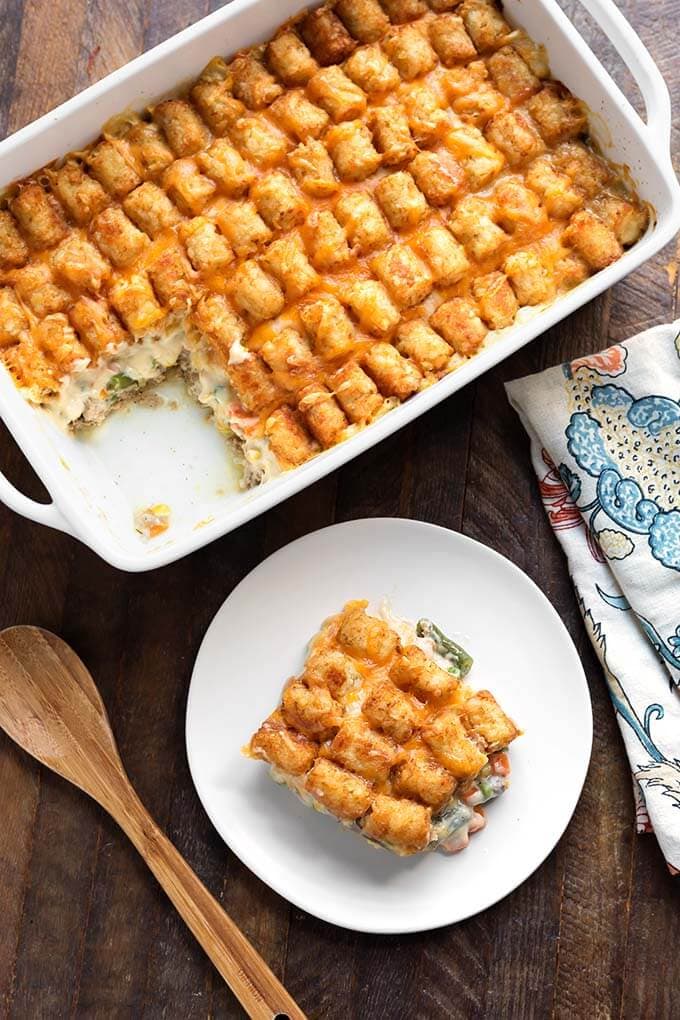 Serving of tater tot casserole on a white plate with more in the baking dish.