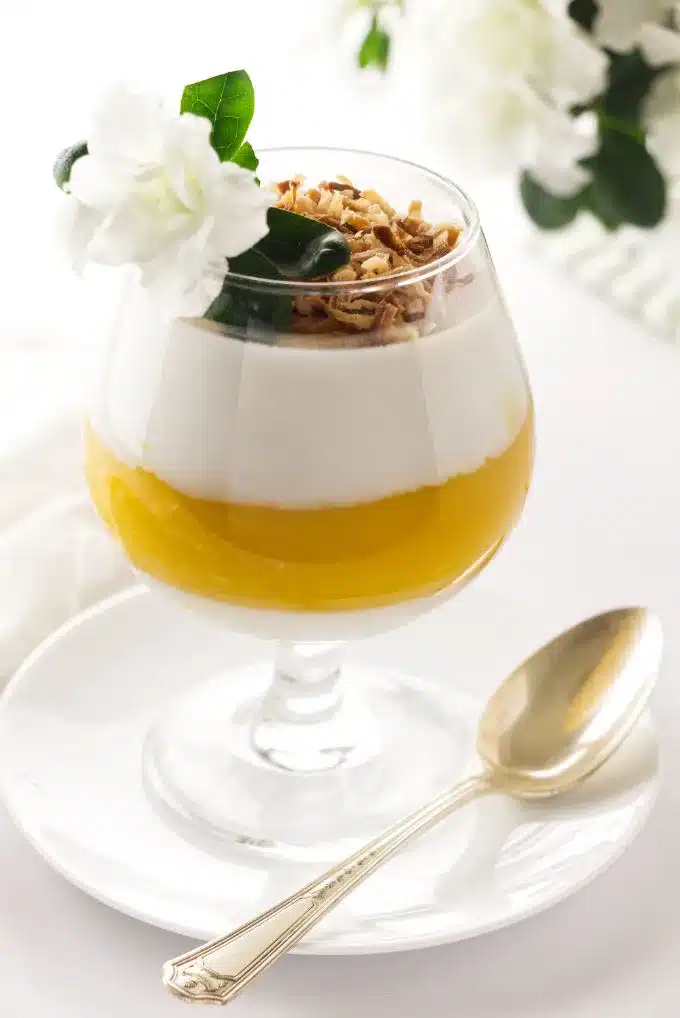 Cup filled with coconut mango panna cotta and toasted shredded coconut on top.