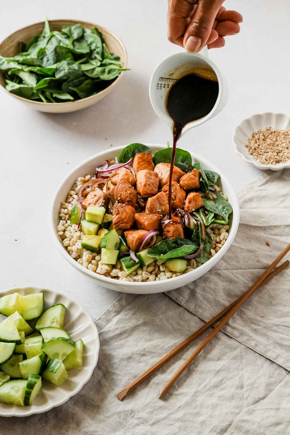 Salmon bowl with diced cucumber, raw spinach, sliced red onions, and barley with hand pouring Teriyaki sauce.