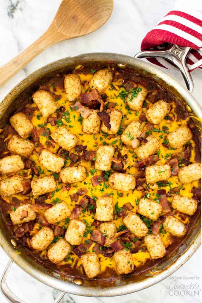 BBQ chicken tater tot casserole in a skillet with wooden spoon and dish towel.