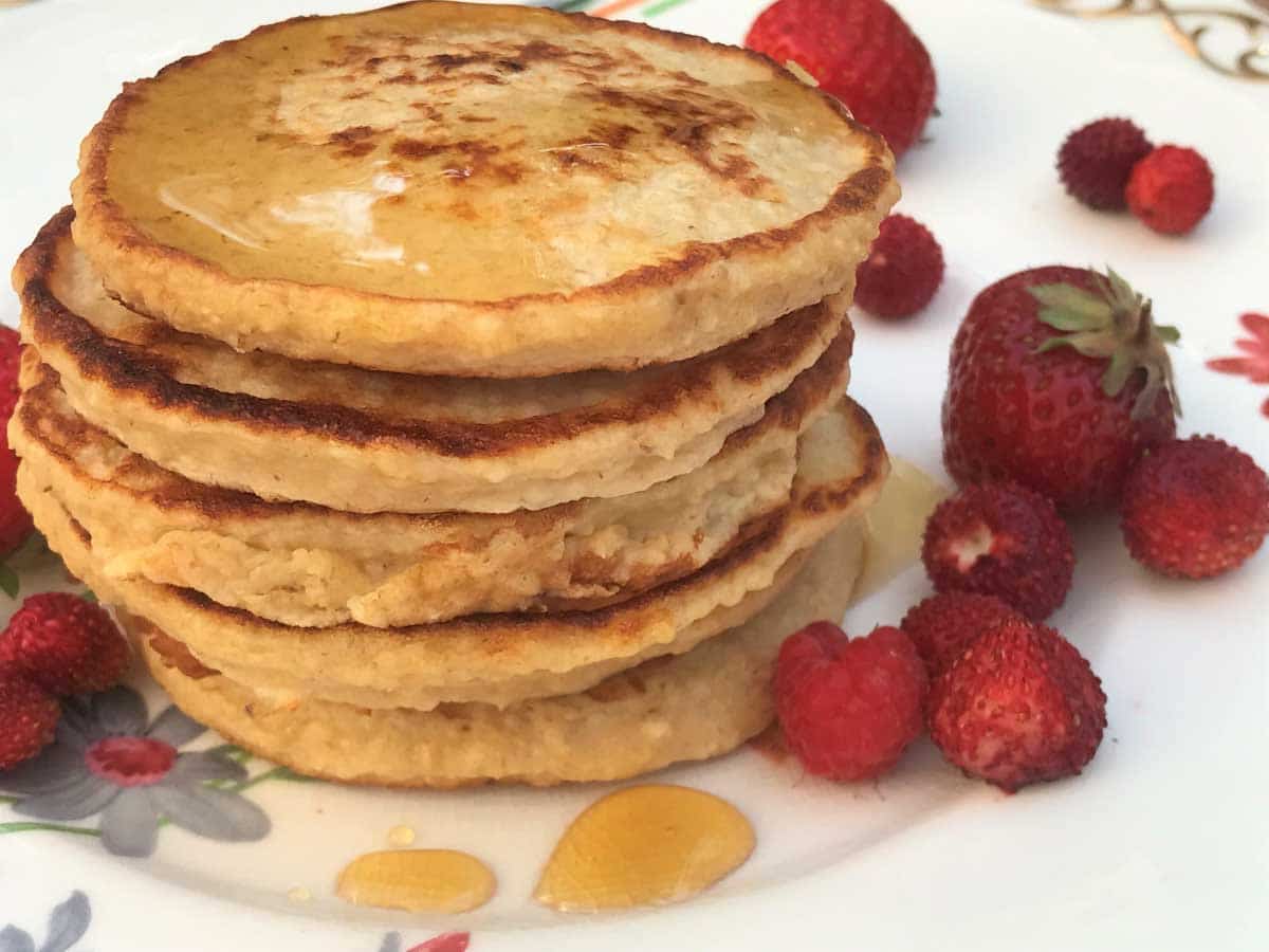 Stack of cottage cheese pancakes with berries on a white plate.