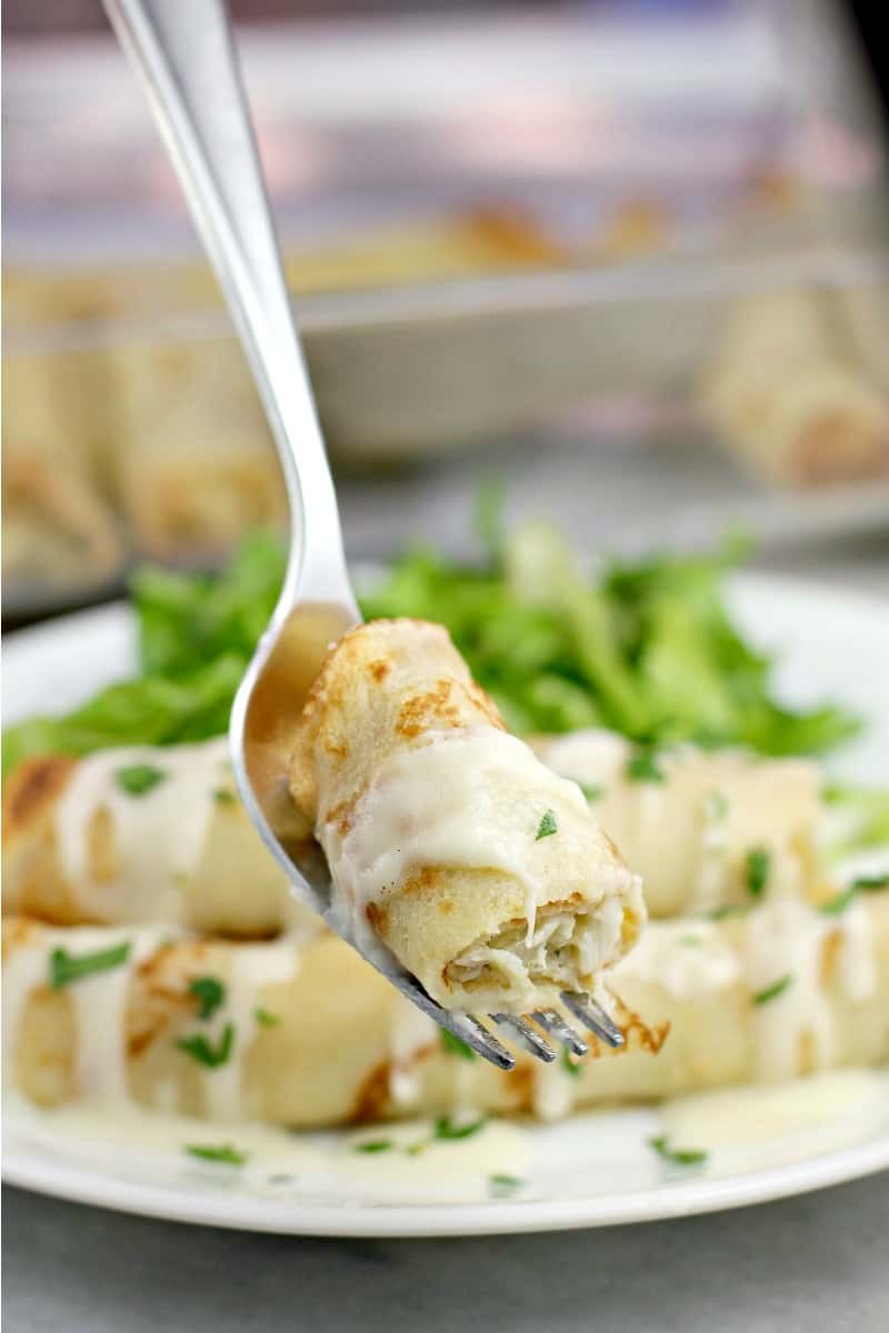 Piece of crab stuffed crepes on a fork with more in the background.