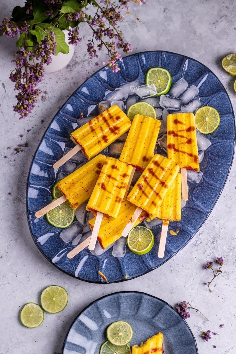 Mango Tajin popsicles on top of ice cubes on a blue platter.