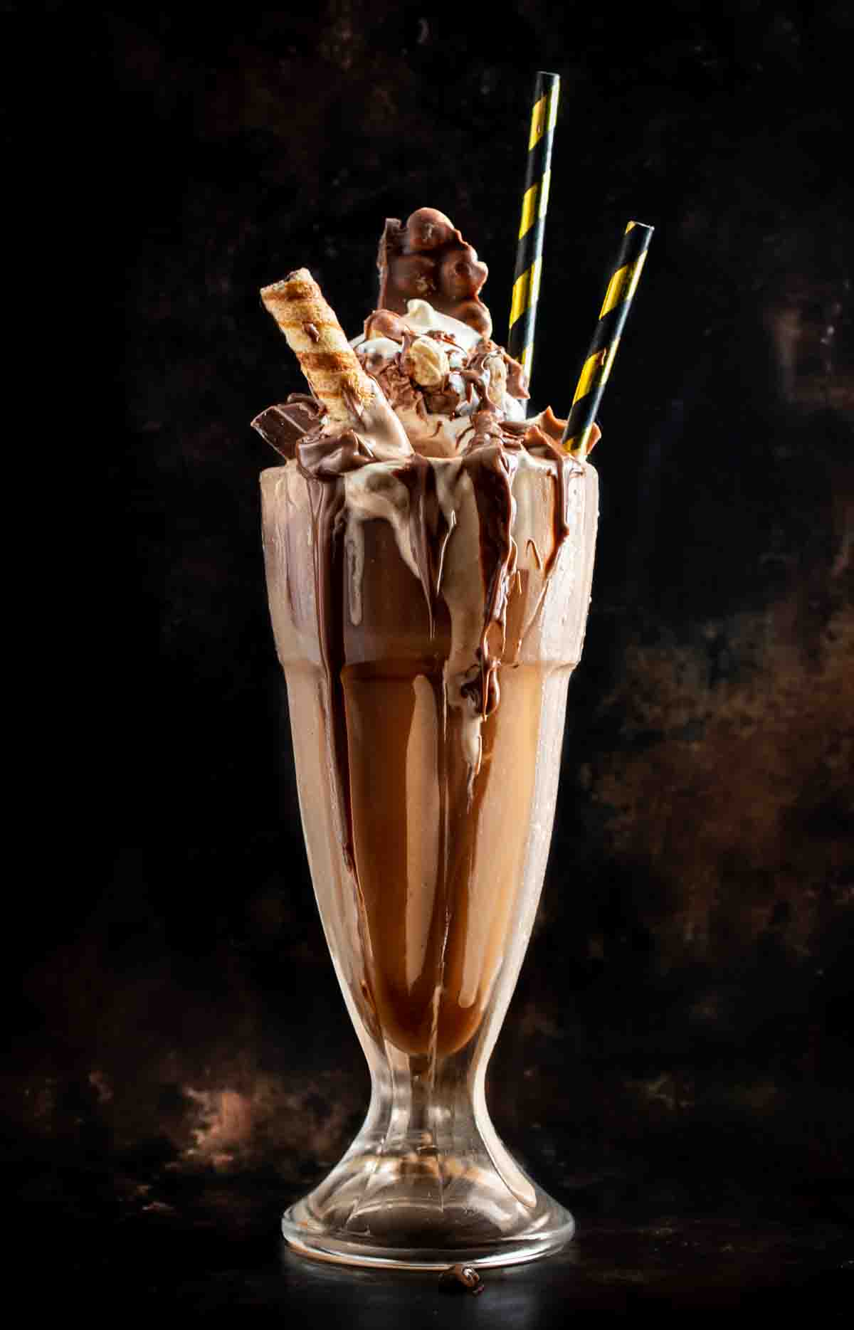 Chocolate shake topped with wafer cookers, chocolate covered hazelnuts and decorative straws.