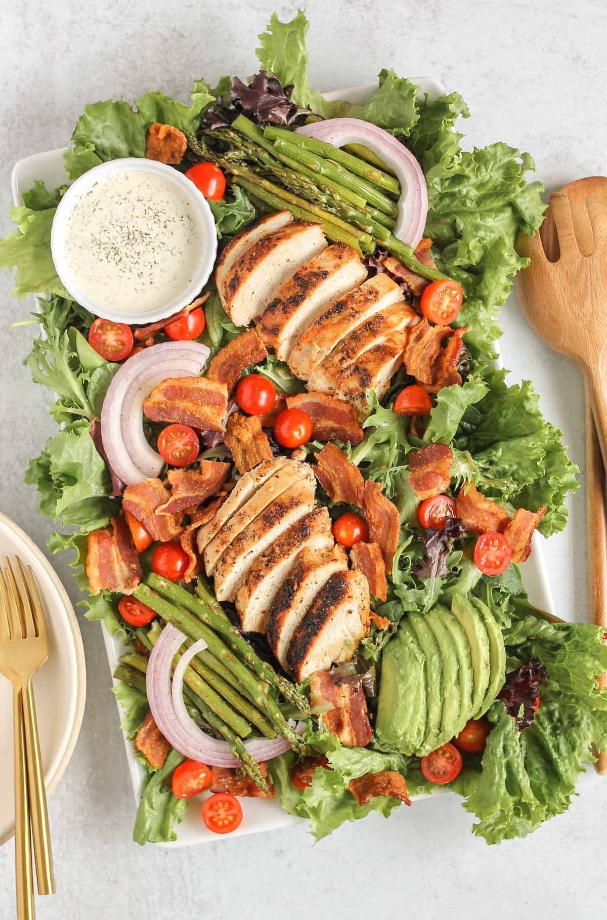 Chicken salad with bacon, cherry tomatoes, red onions, lettuce, asparagus and dressing on a platter.