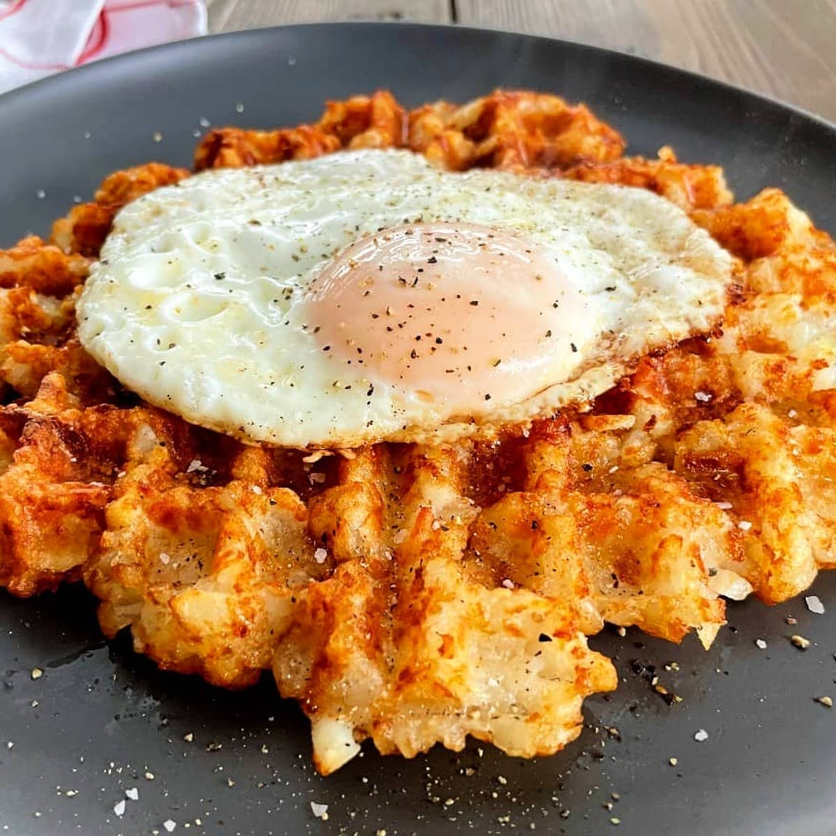 Waffle iron tater tots with fried egg on a dark gray plate.