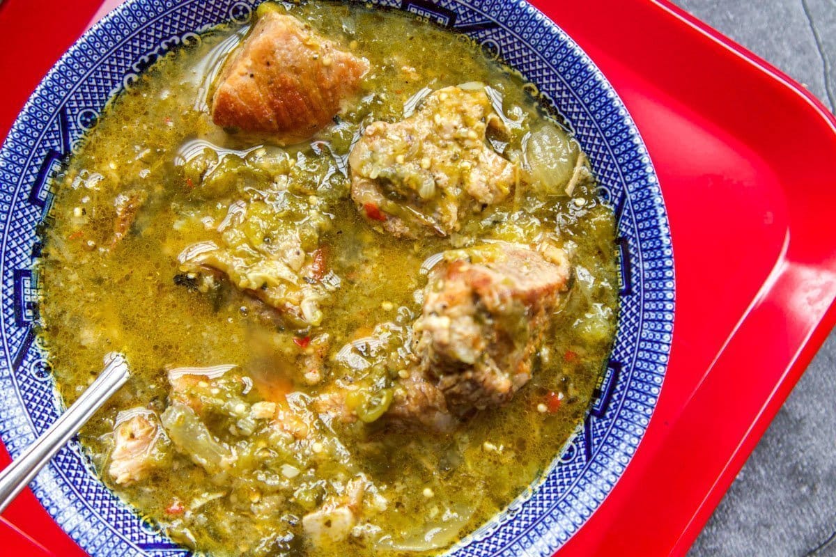 Serving of chili verde in a decorative blue bowl on a red tray.