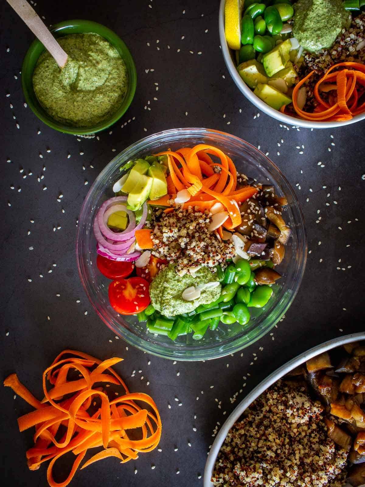 Clear bowl with quinoa, shaved carrots, diced avocado, red onions, edamame, and tomatoes.
