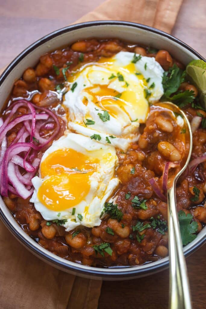 Smoky beans with eggs and pickled red onion in a pot.