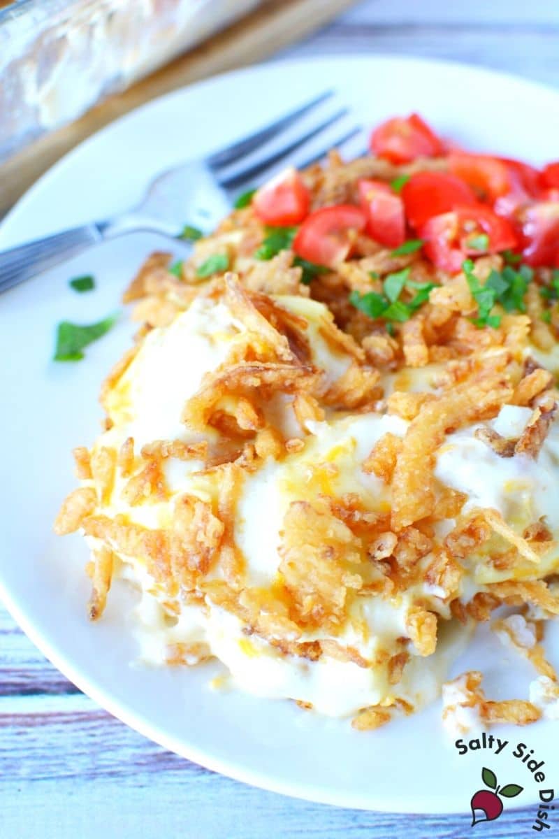 Serving of cream of chicken tater tot casserole with tomatoes and herbs on a white plate with fork.