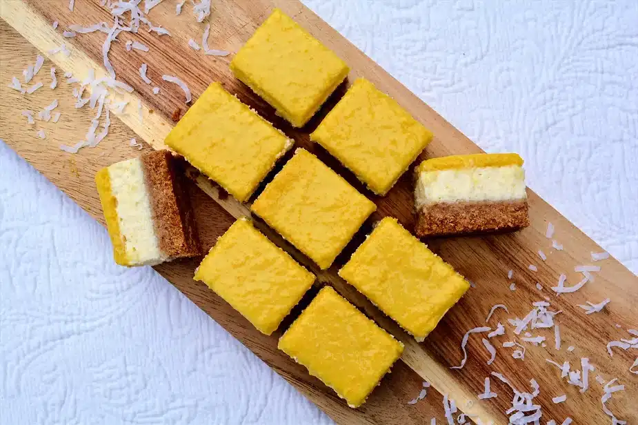 Mango coconut cheesecake bars cut on a wooden board.