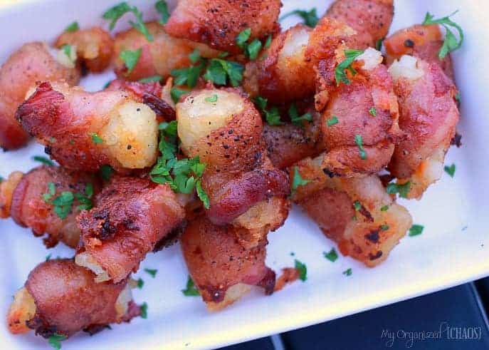 Bacon cheese stuffed bacon wrapped tater tots on a white platter.