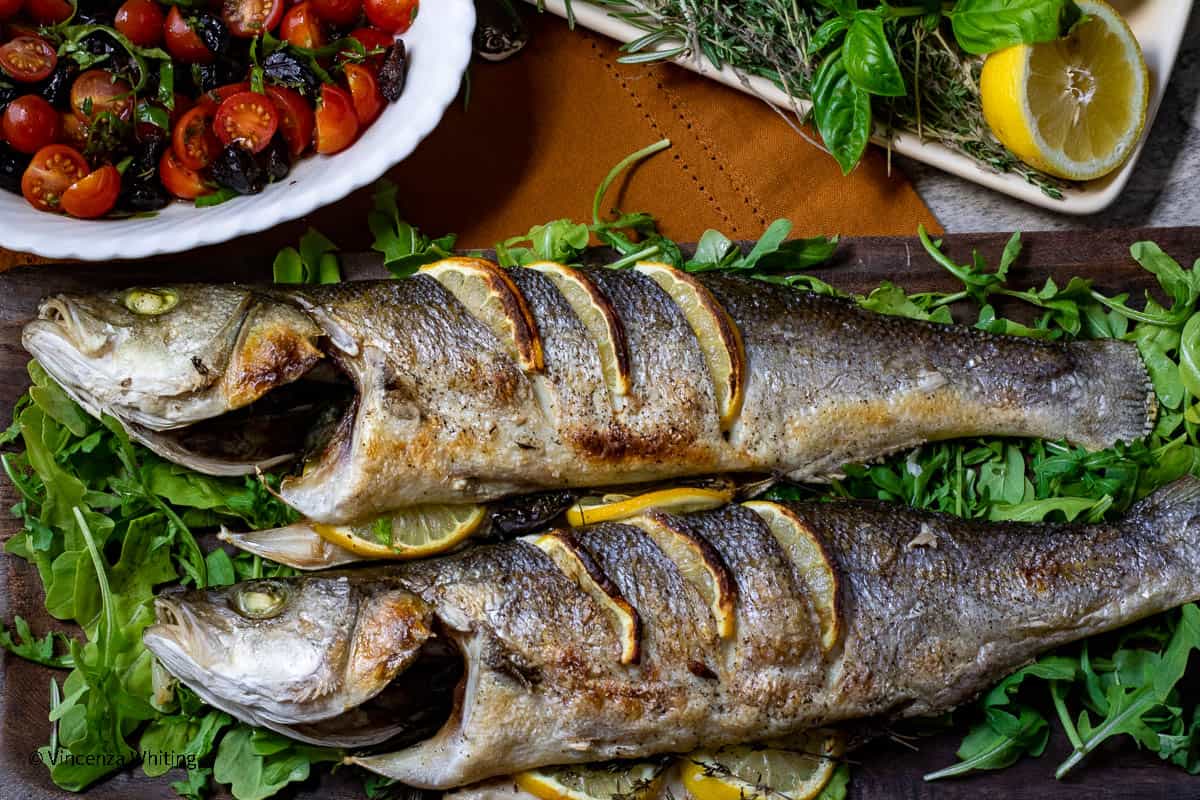 Whole roasted Branzino with tomato and olive salad on a bed of arugula.