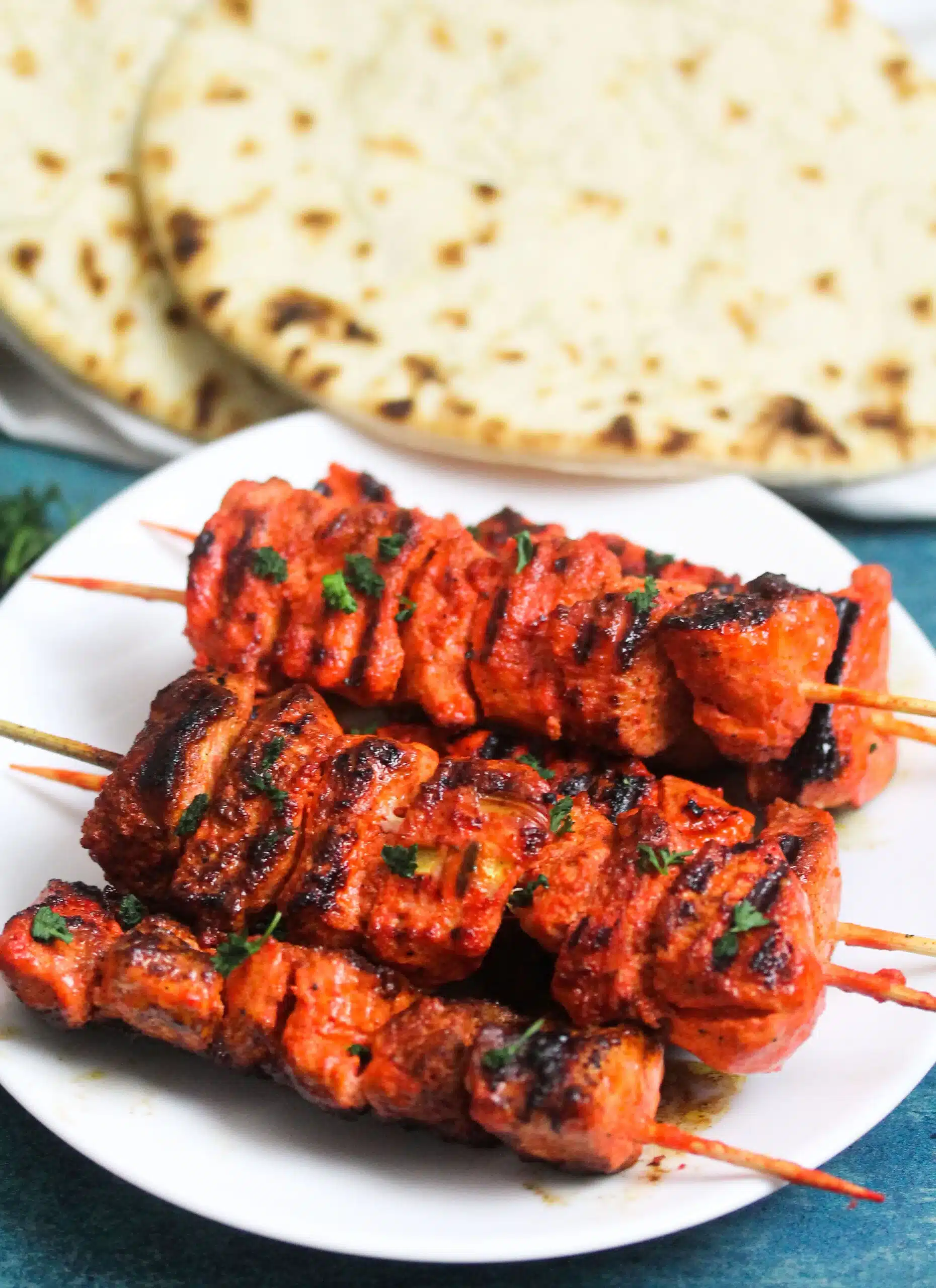 Indian Tandoori chicken kebabs on a white plate with naan bread in the background.