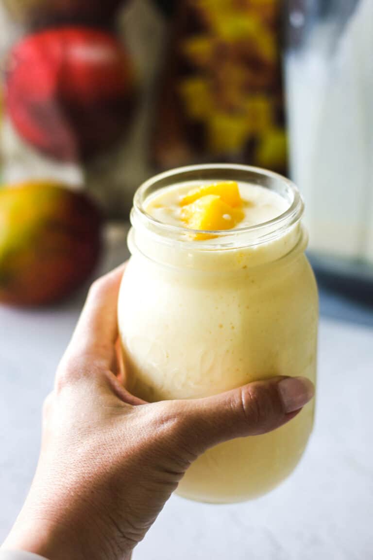 Hand holding a mason jar with mango lassi.