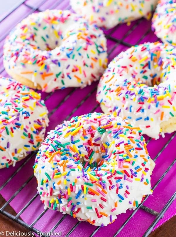 Baked vanilla donuts with colorful sprinkles on a black rack.