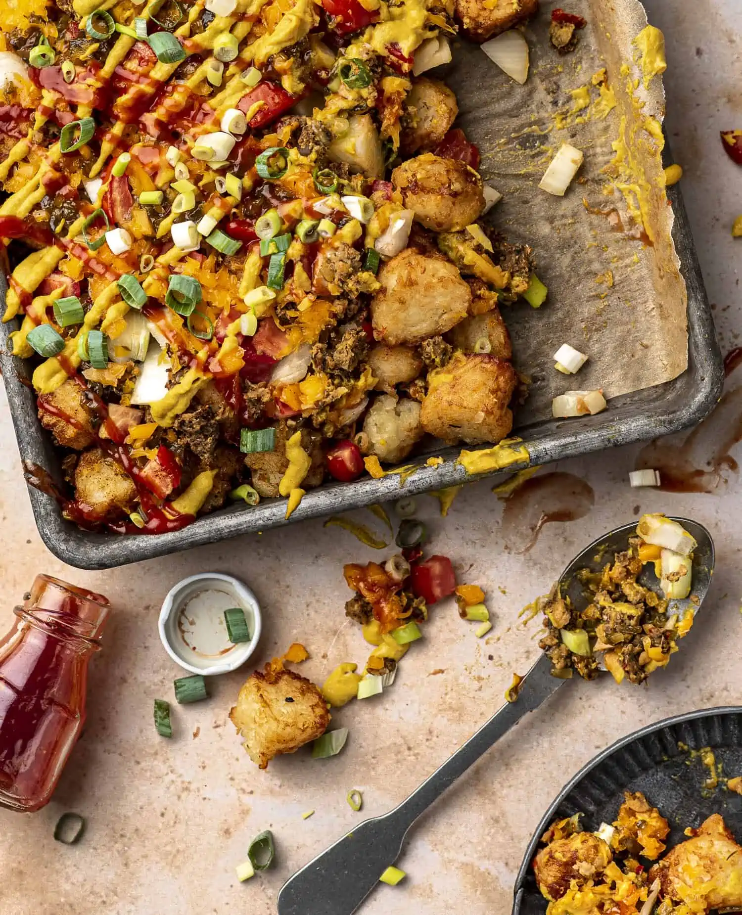 Vegan burger tater tots on a parchment lined sheet pan with serving spoon and ketchup in the background.