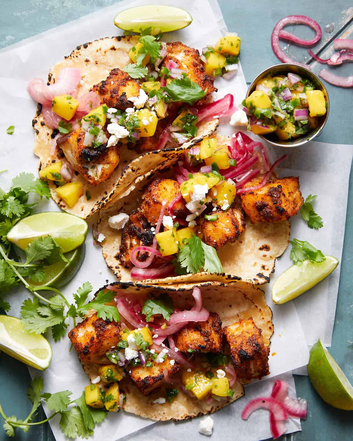 Fish tacos with lime wedges and mangoes.
