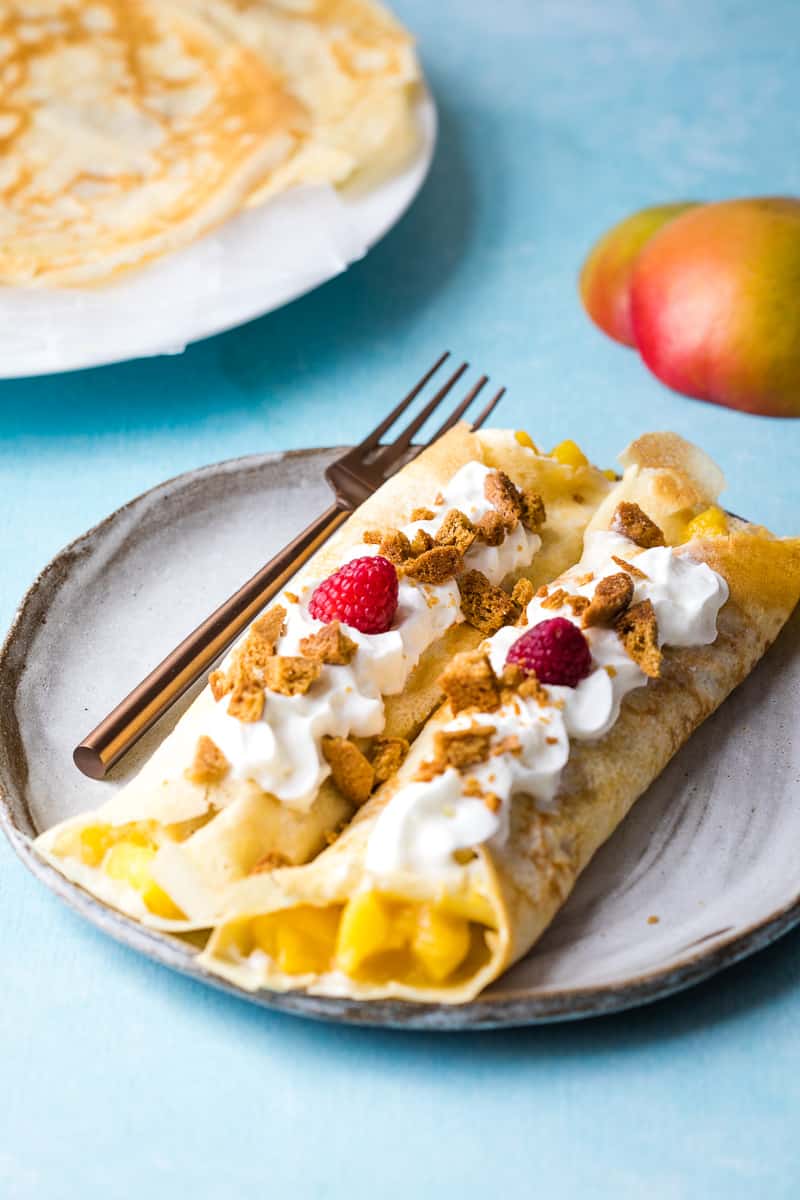 Sweet mango crepes with mango filling topped with whipped cream, crushed ginger cookies and raspberries.