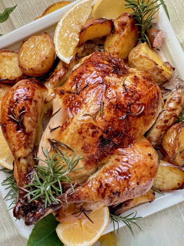 Rosemary citrus roast chicken with roasted potatoes on a white platter.