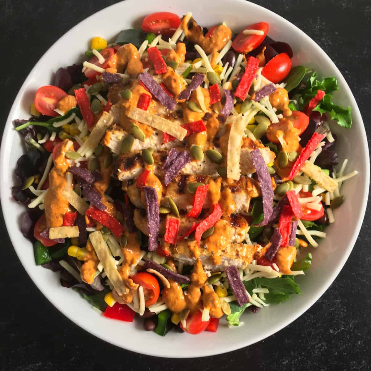 Spicy Southwest chicken salad with tortilla strips , pepitas, tomatoes, cheese, and dressing.