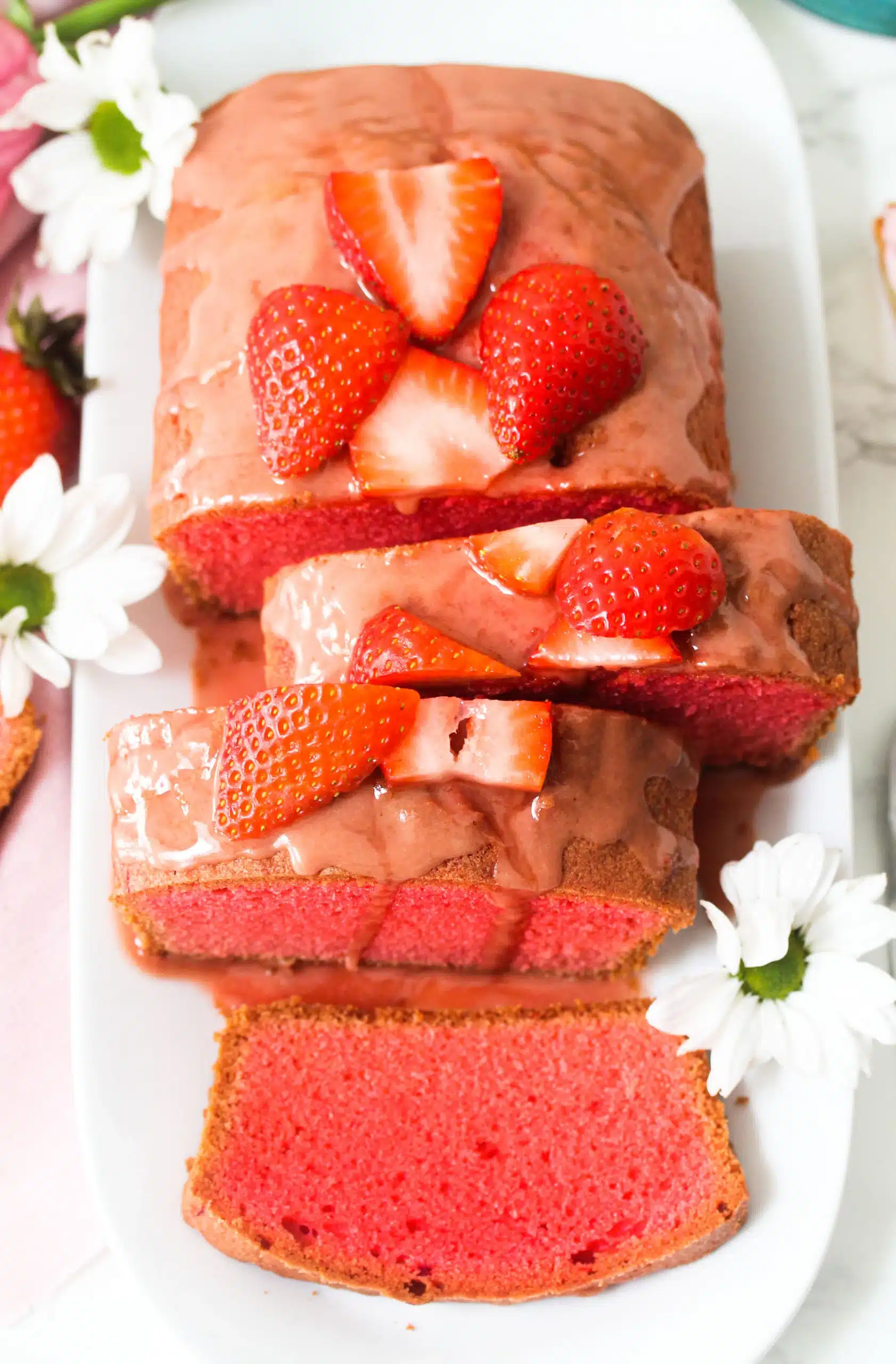 Sliced strawberry pound cake with white flowers on a white platter.