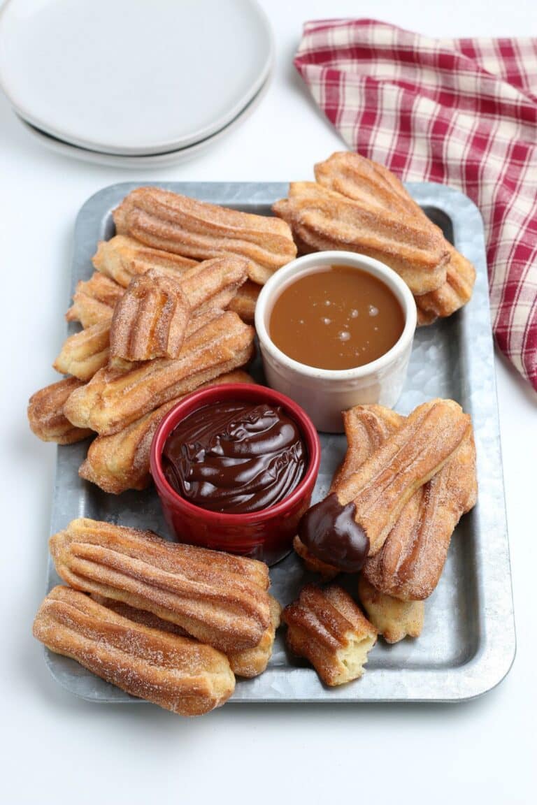 Air fryer churros on a silver platter with chocolate and caramel sauce.