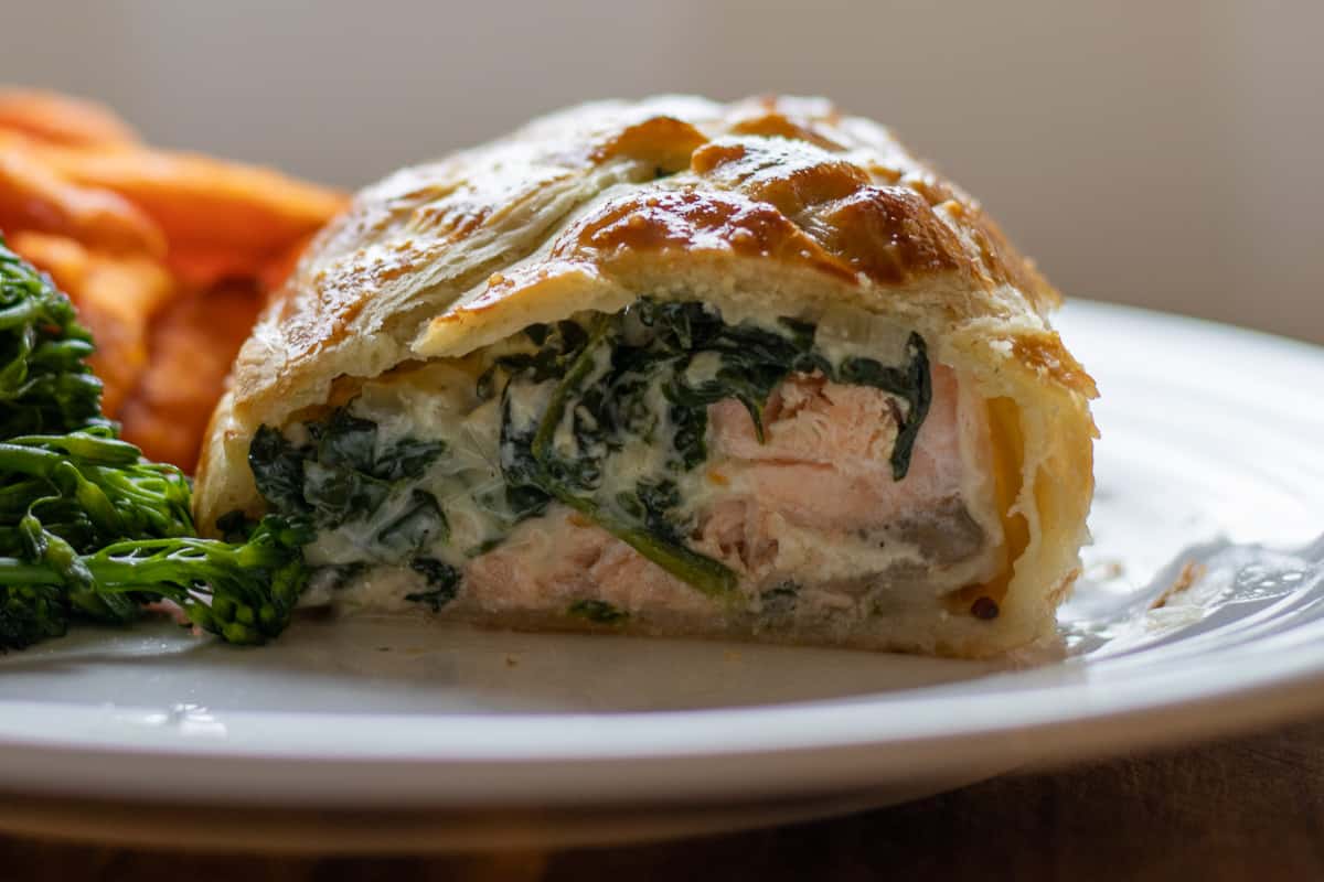 Individual salmon en croute with broccoli and sweet potatoes on a white plate.