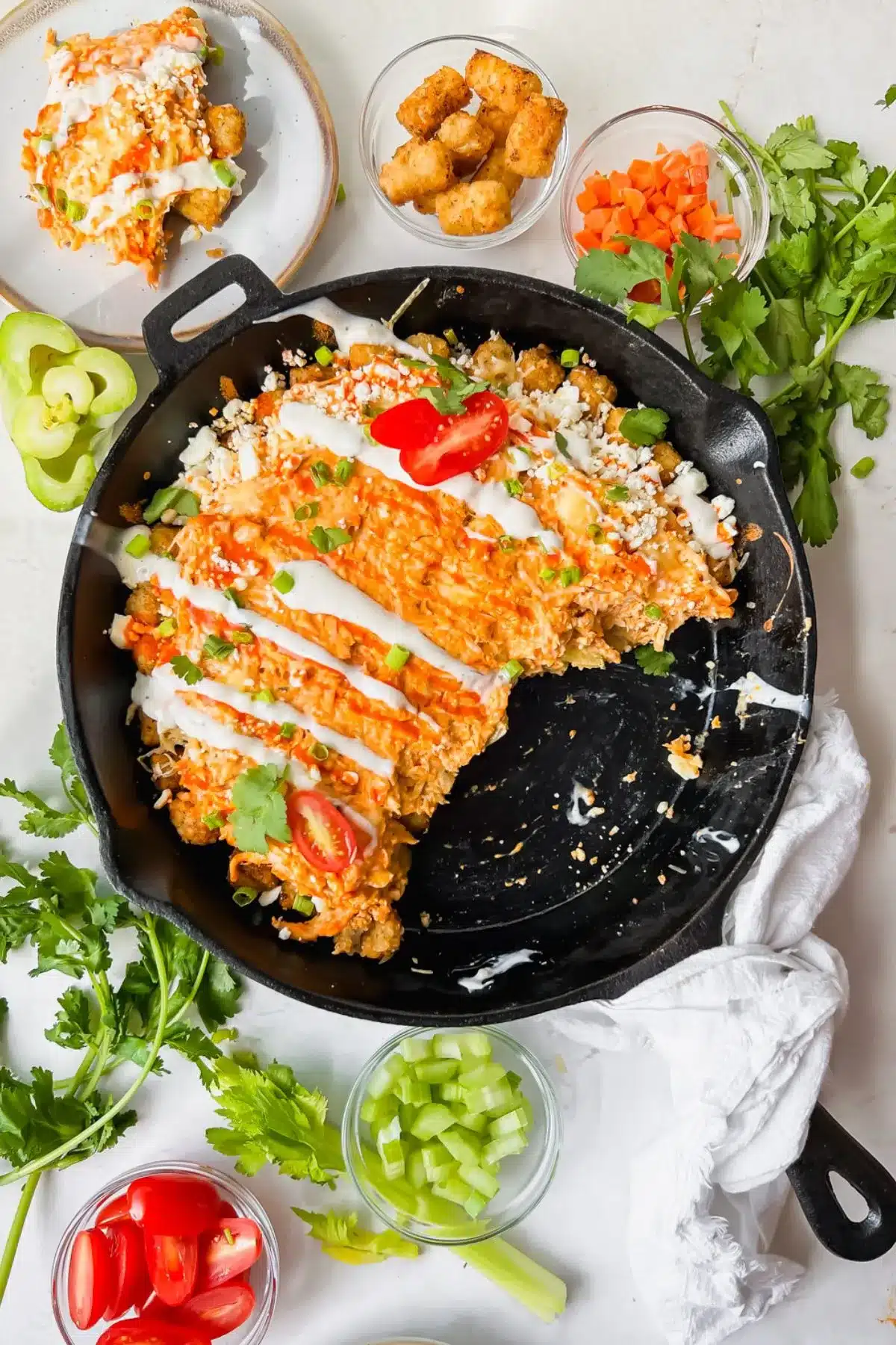 Buffalo chicken totchos in a cast iron pan with ingredients around it.