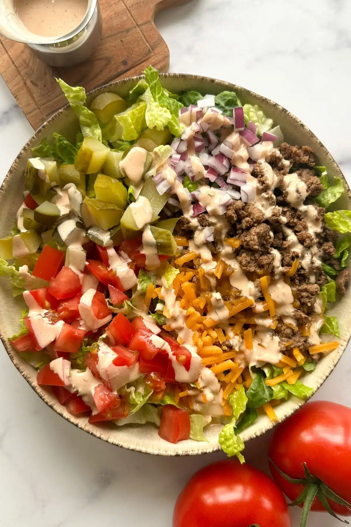 Cheeseburger bowl with ground beef, red onion, diced pickles, tomatoes, shredded cheese, and lettuce.