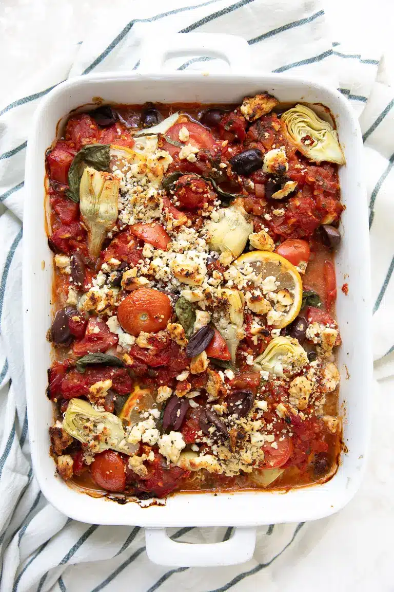 Mediterranean baked fish with artichokes and olives in a white baking dish.