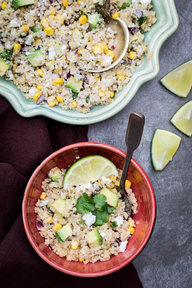 Quinoa avocado salad with corn in a fancy platter with a serving in a small red bowl.