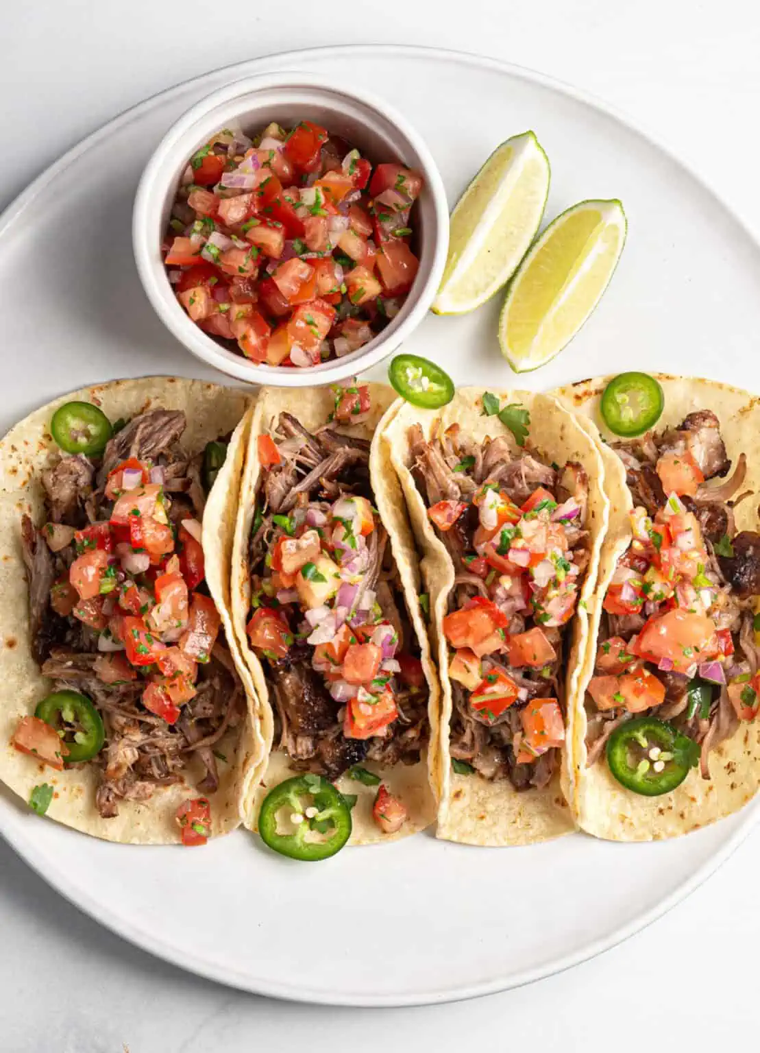 Instant Pot carnita tacos with lime wedges and salsa on a white plate.