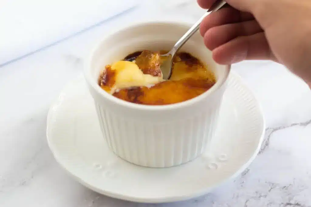 Hand dipping spoon into creme brulee.