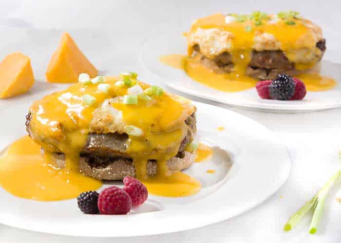 Two servings of Wisconsin eggs benedict with beer cheese sauce with berries on white plates.