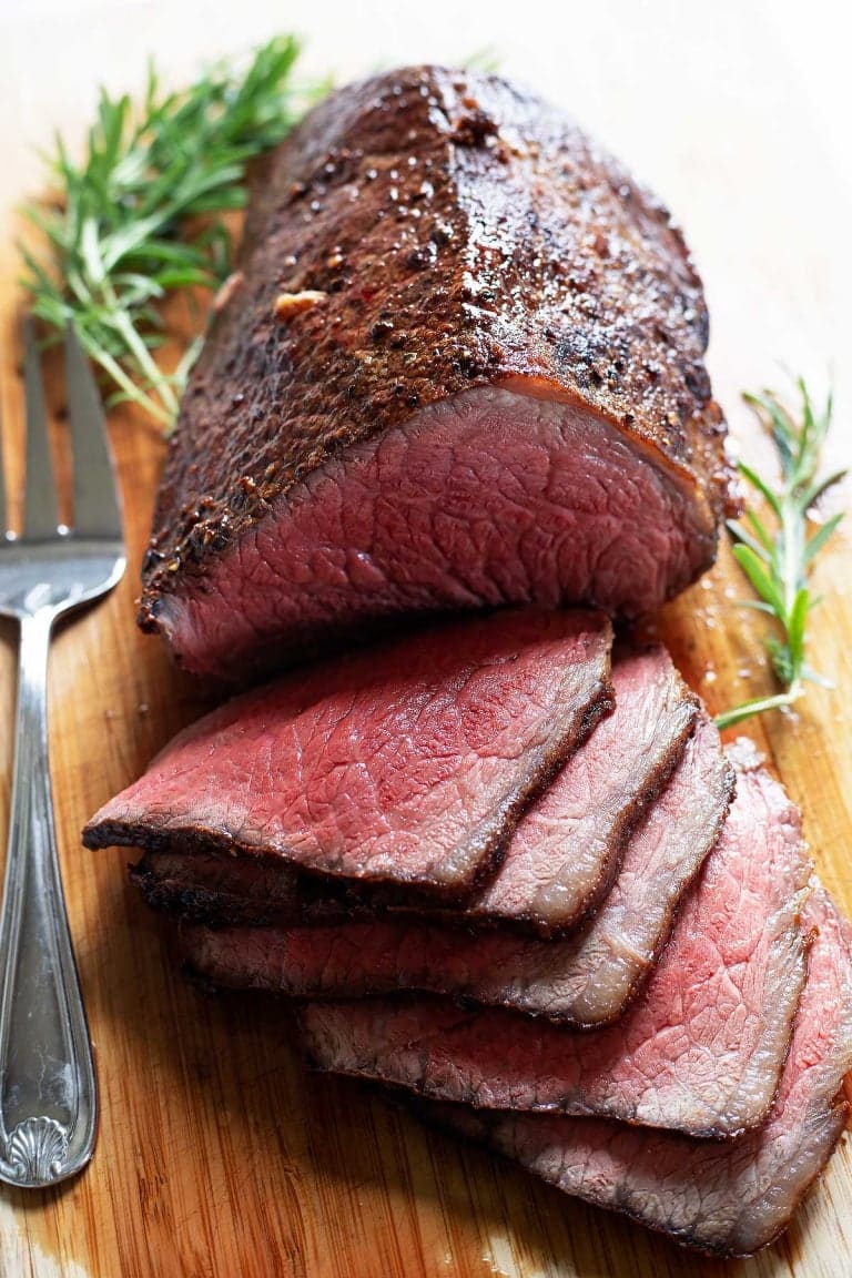 Sliced roast beef on a wooden cutting board.