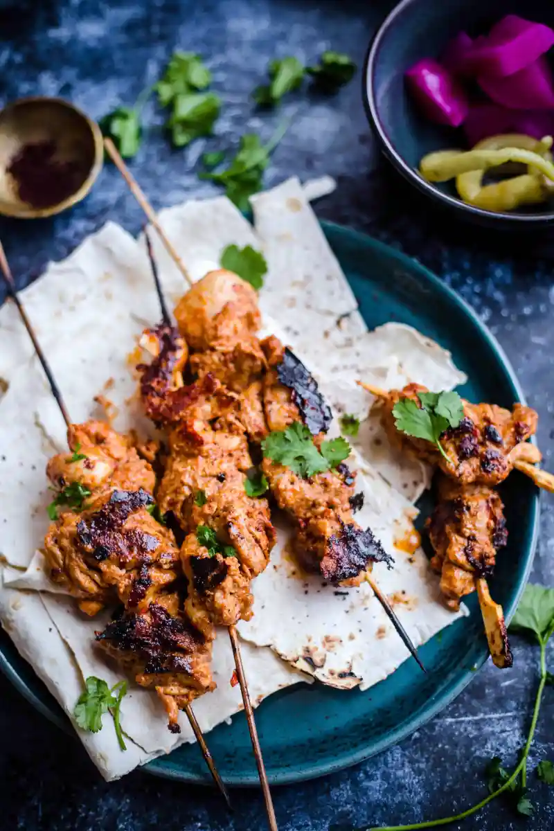 Shish Tawook skewers on a parchment lined blue plate.