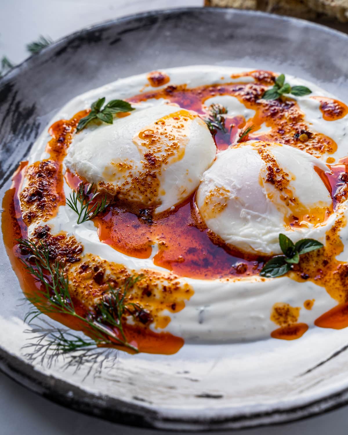 Greek yogurt with poached eggs with herbs and spiced butter on a decorative plate.