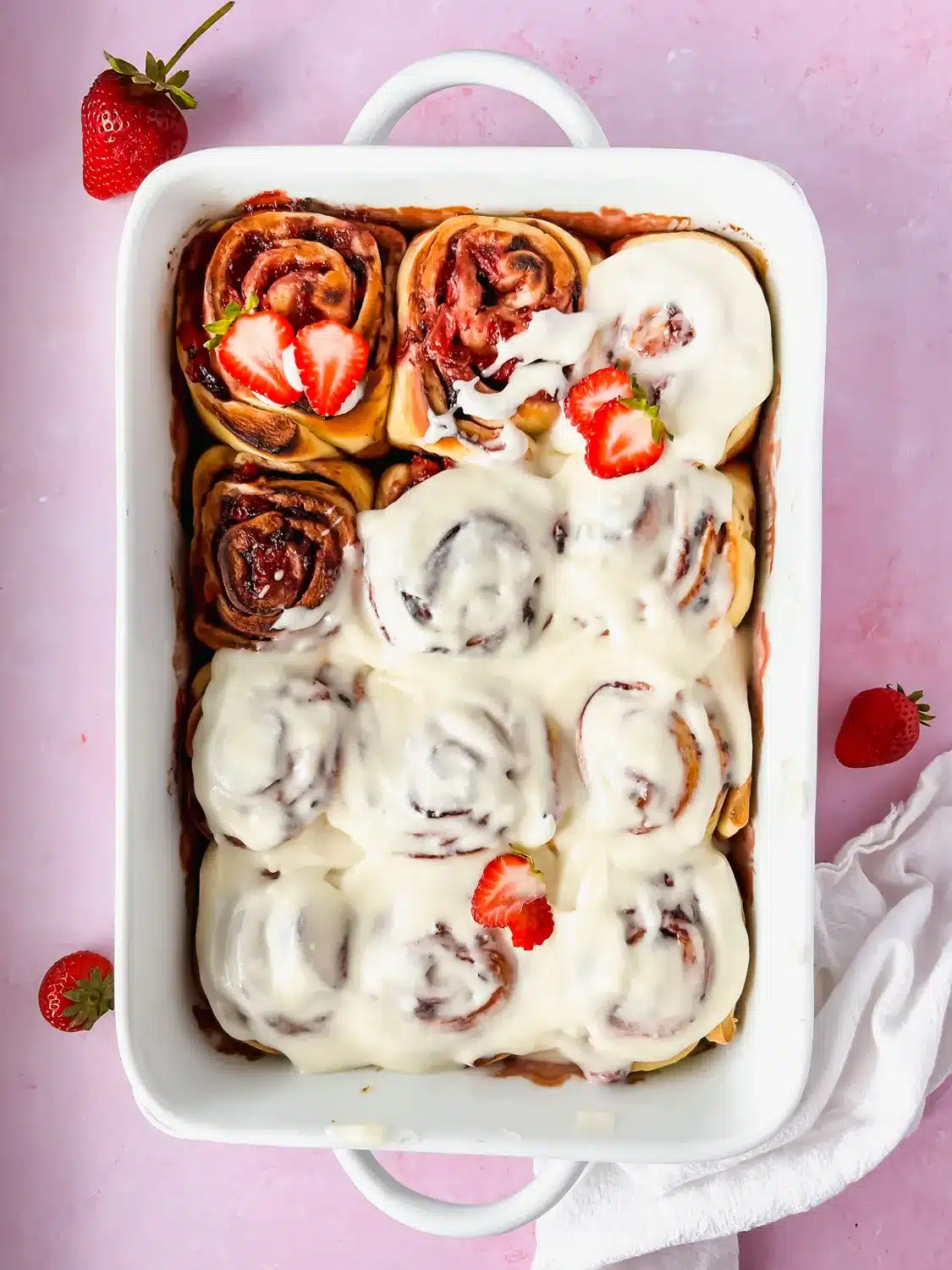 Strawberry cinnamon rolls in a white baking dish with fresh strawberries.