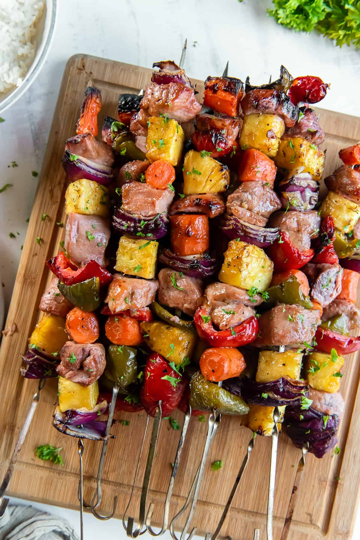 Sweet and sour pork kababs with pineapple, bell peppers, and carrots on a wooden cutting board.