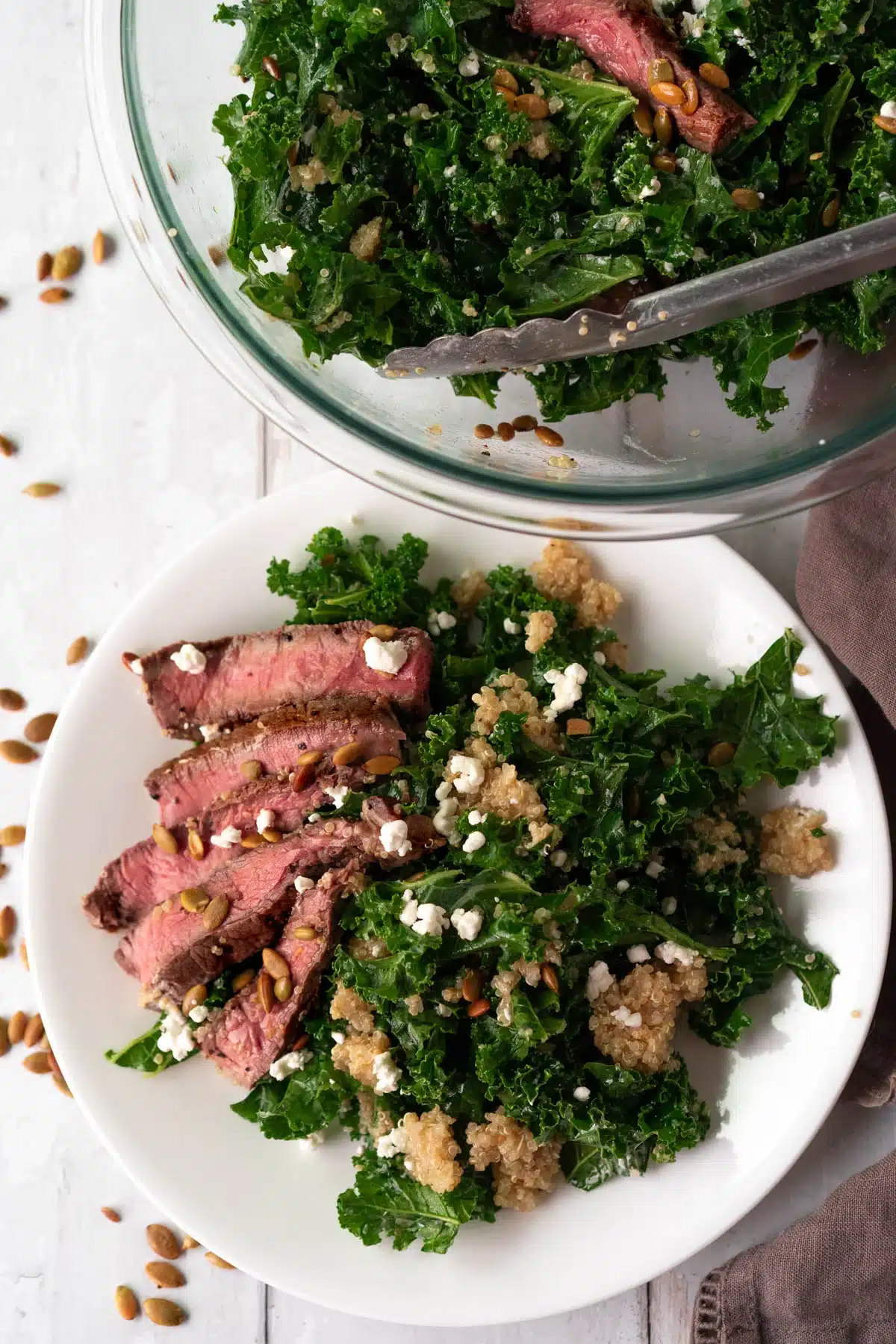 Kale and quinoa with steak on a small white plate.