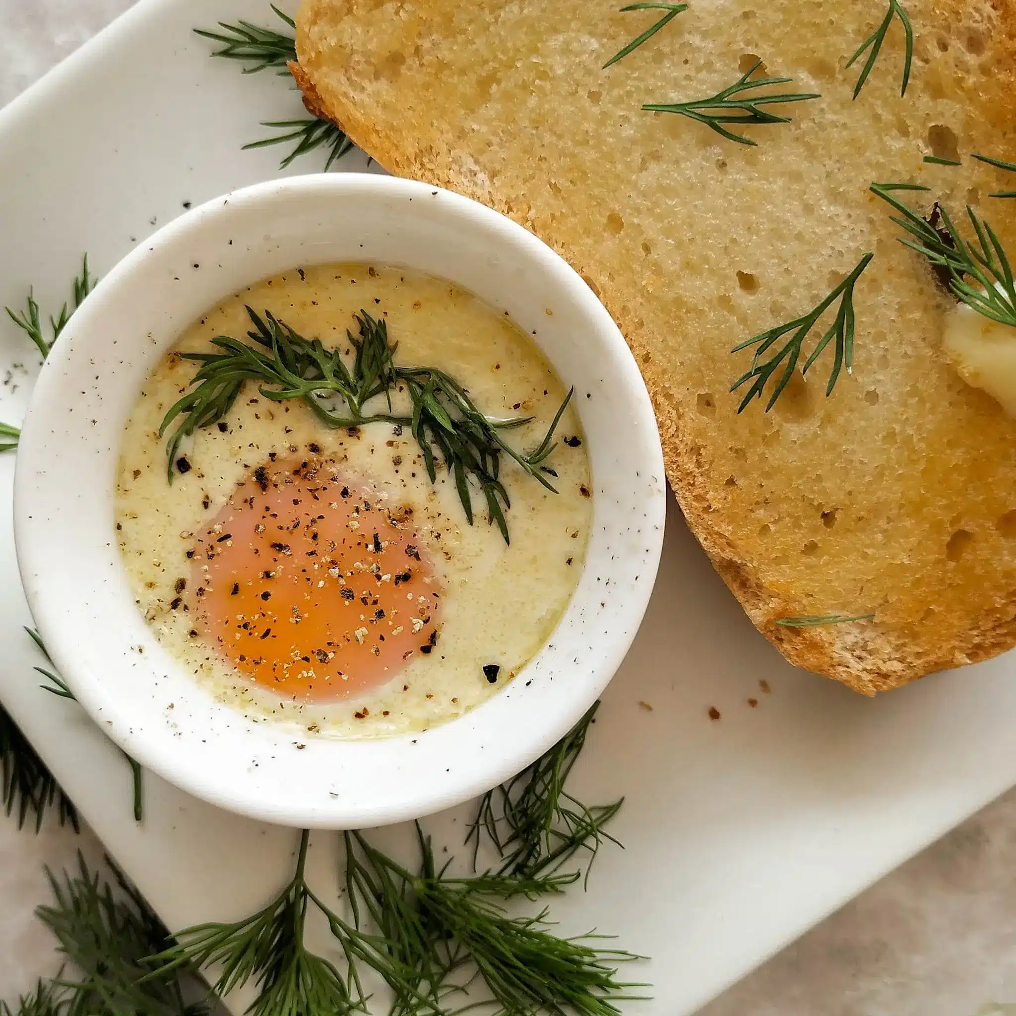 French baked egg in a ramekin with herbs and buttered toast.