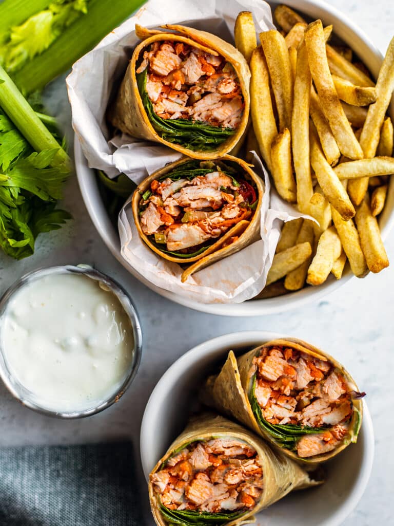 Buffalo chicken wraps, sliced in half, with fries and blue cheese dressing.